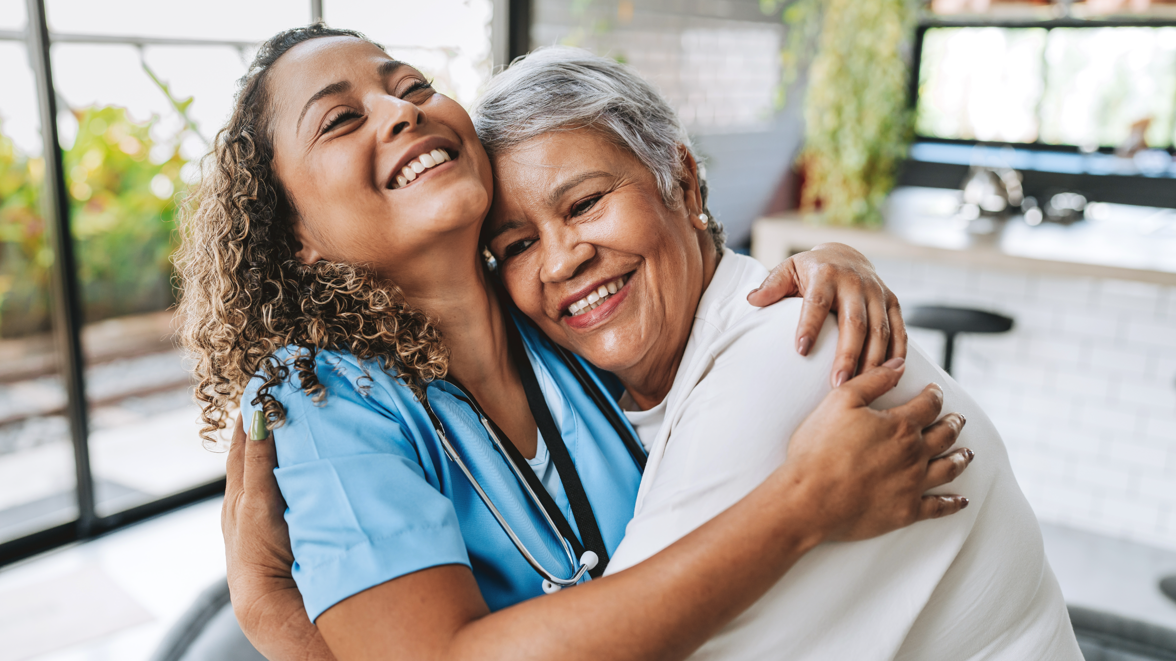 Home health nurse and an older woman embracing warmly in a bright kitchen