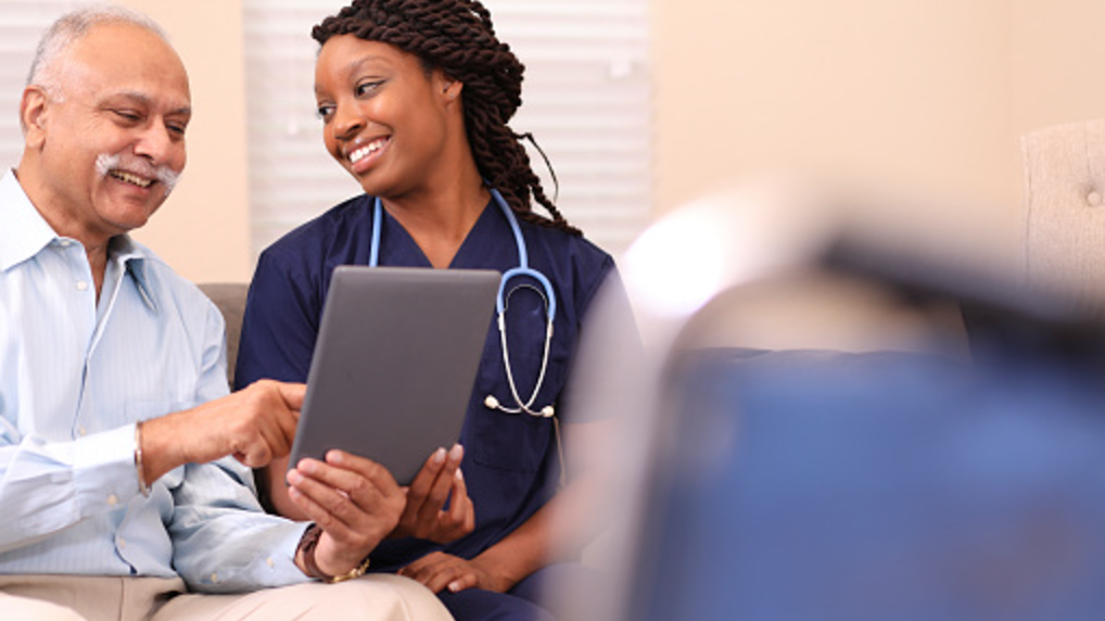 Nurse reviewing health readings on a tablet with an older man at his kitchen table